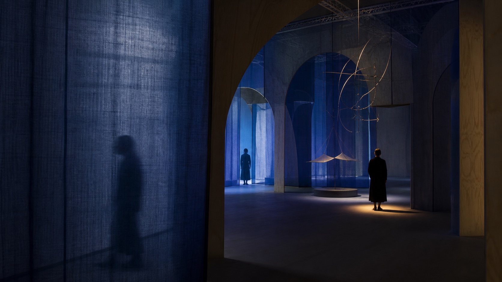 La scénographie achevée mêle voiles indigo, bois courbe et lumière ambrée